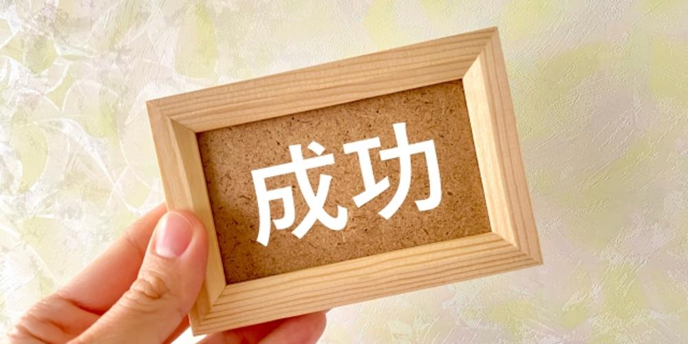「成功」の文字が書かれた木製フレームを手に持つイメージ写真(ビジネス・目標達成の象徴)