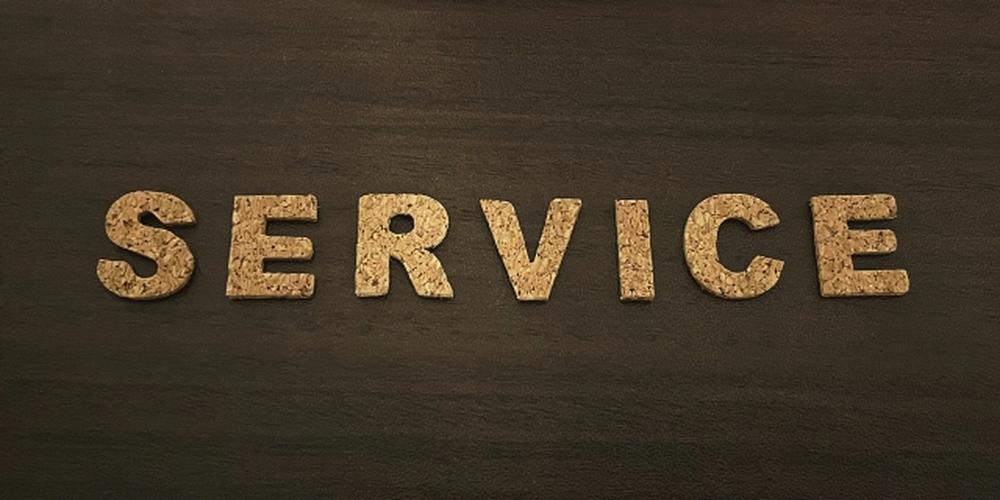 暗い木目の背景にコルク素材で並べられた「SERVICE」の文字と赤いミニカー、サービスやサポートの概念を表す構図