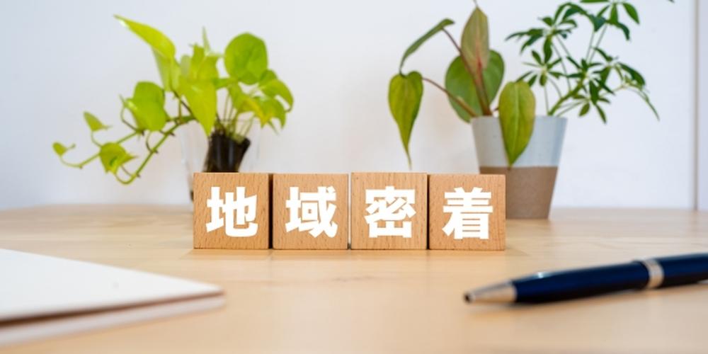 地域密着の不動産サービスをイメージした木製ブロックと観葉植物の背景