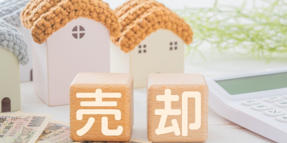 家のミニチュアと「売却」の木製ブロック、電卓
