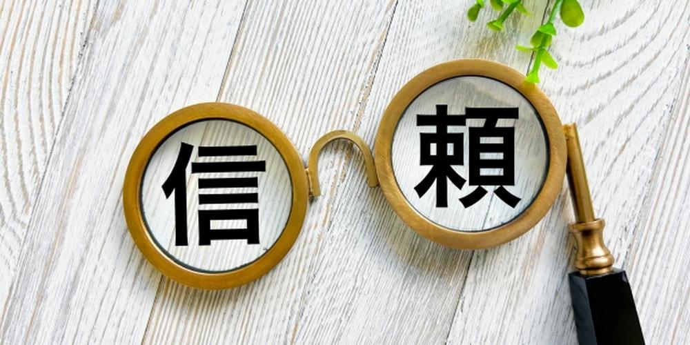 信頼を表す文字がレンズ型のフレームに表示されたイメージ。木目調の背景と観葉植物が添えられている。