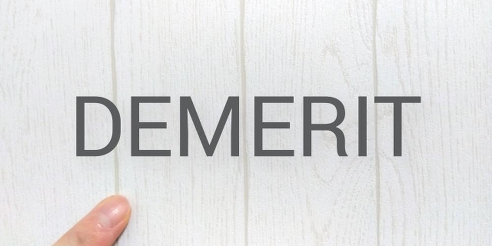 白い木目調の背景に「DEMERIT」の文字と指先が映るシンプルな構図、デメリットや短所を示すイメージ