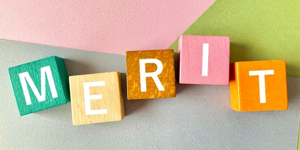 「カラフルな木製ブロックで並べられた“MERIT”の文字とパステルカラーの背景」