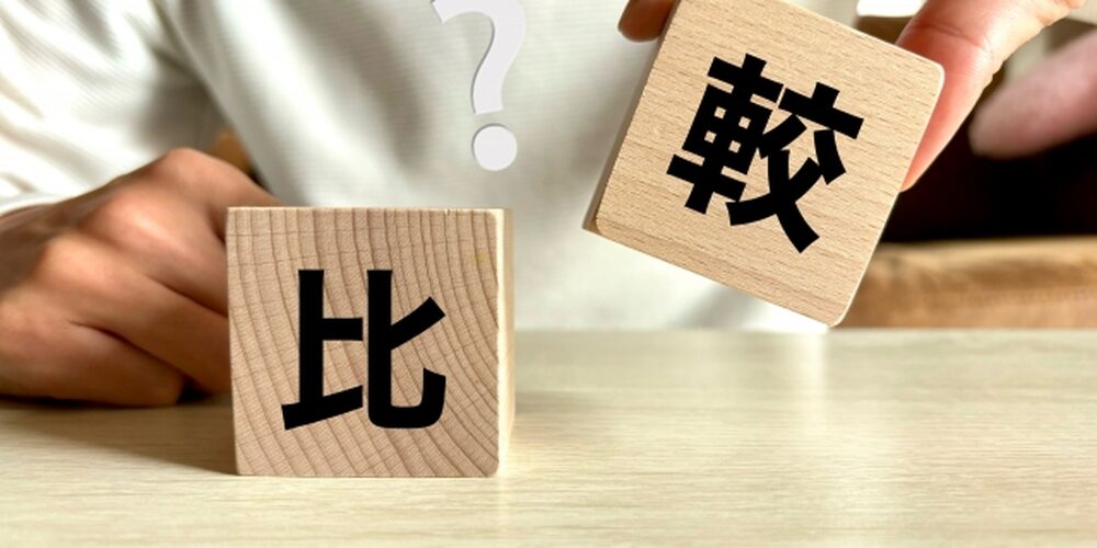 木製ブロックに「比較」の漢字が書かれた画像。左が「比」、右が「較」で、背景にはクエスチョンマークが浮かぶシーン