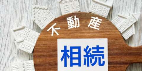 不動産相続に関するイメージ画像。家の模型と木製のボードに『不動産 相続』の文字。